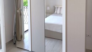 Ein modernes Schlafzimmer mit einem großen Spiegel, einem Bett mit weißer Bettwäsche und einem Balkon mit Vorhang.
