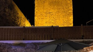 Terrassa exterior amb mur de pedra, una piscina, taula de fusta i un parasol negre.
