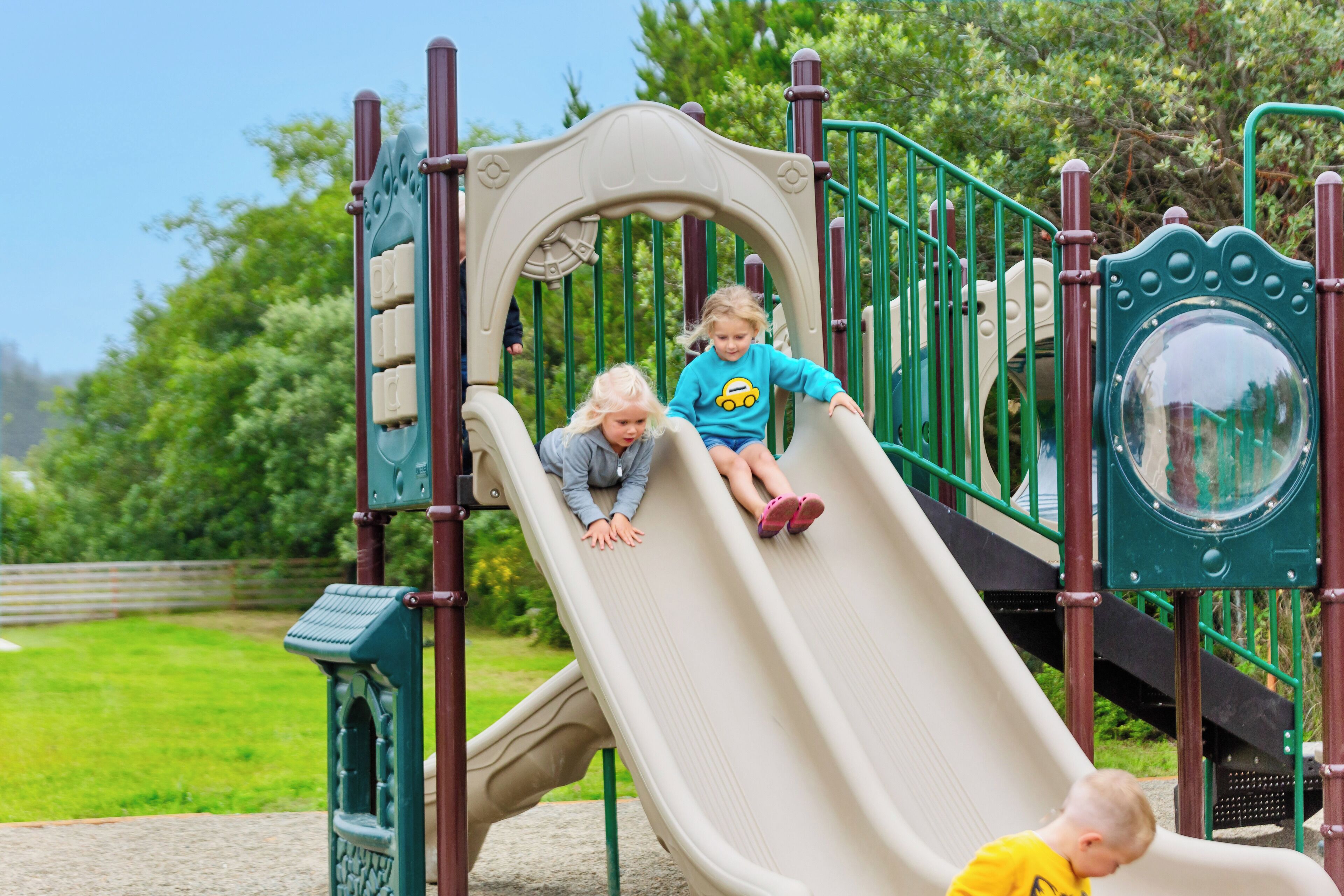 A playground with a slide, climbing structures, and a green fence.
