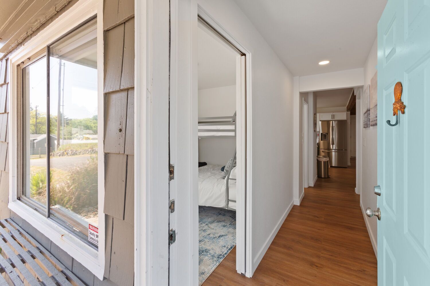 A modern interior with a bunk bed, a kitchen with stainless steel appliances, and a view through a window.