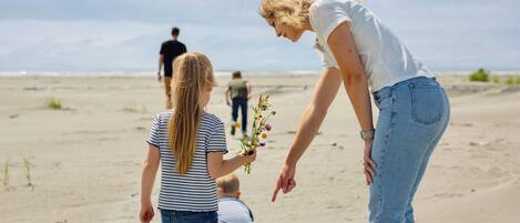 A sandy beach with people, including a woman bending over a child holding flowers.