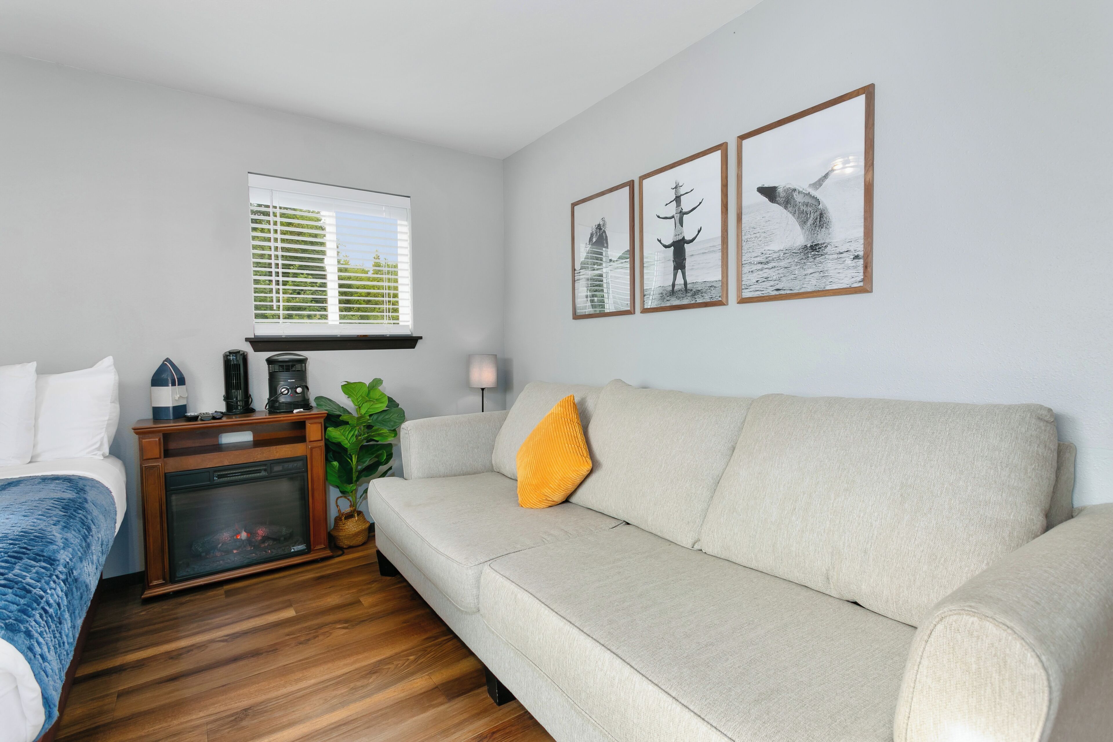 A modern living room with a beige sofa, a blue blanket on a bed, a fireplace, and three framed pictures on the wall.