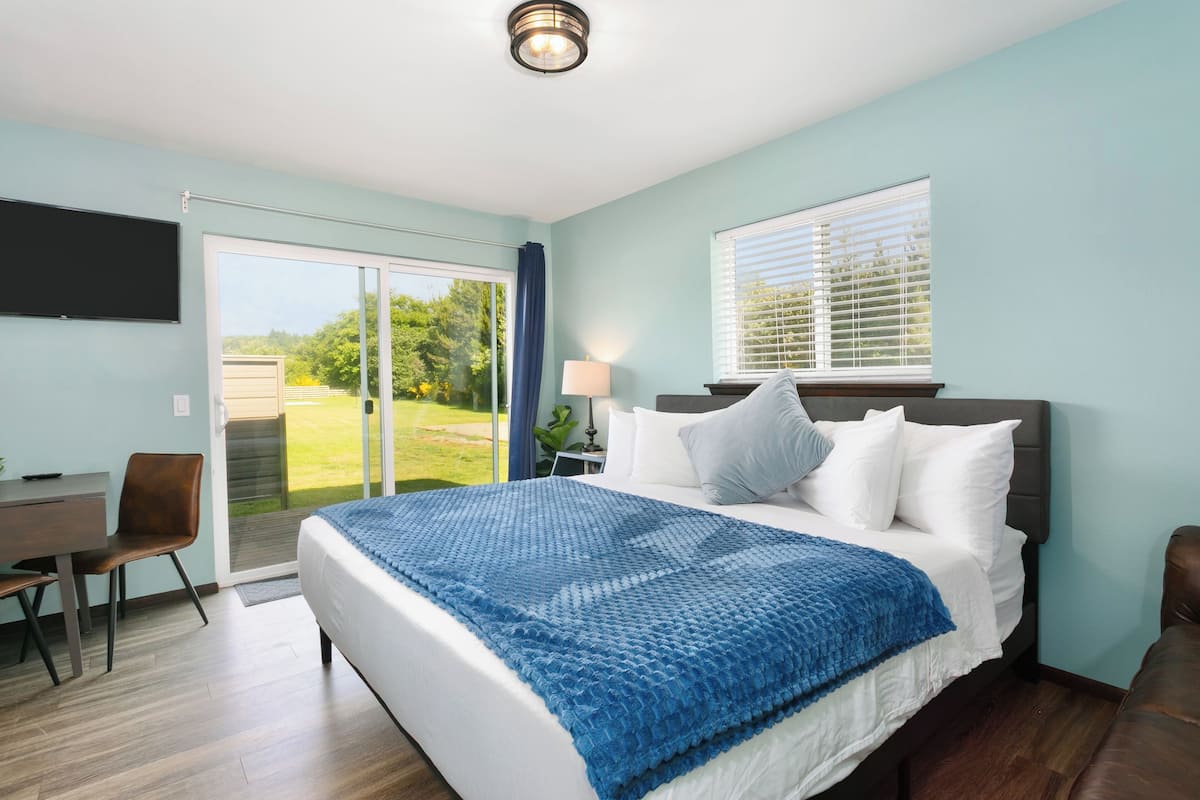 A bedroom with a large bed, a desk, and a chair. There is a sliding glass door leading to a balcony.