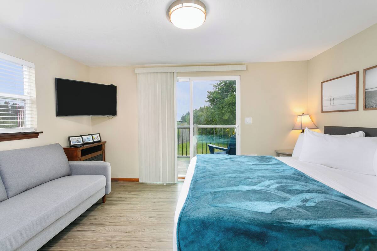 A hotel room with a bed, a sofa, a TV, a balcony, and a lamp.