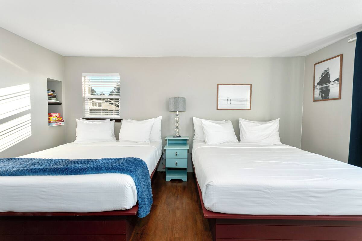 A double room with two beds, a small table, and a window with blinds.