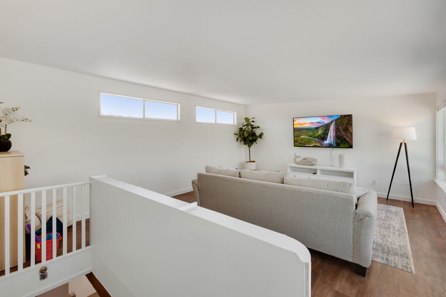 A modern living room with a grey sofa, a flat-screen TV, and a large window.