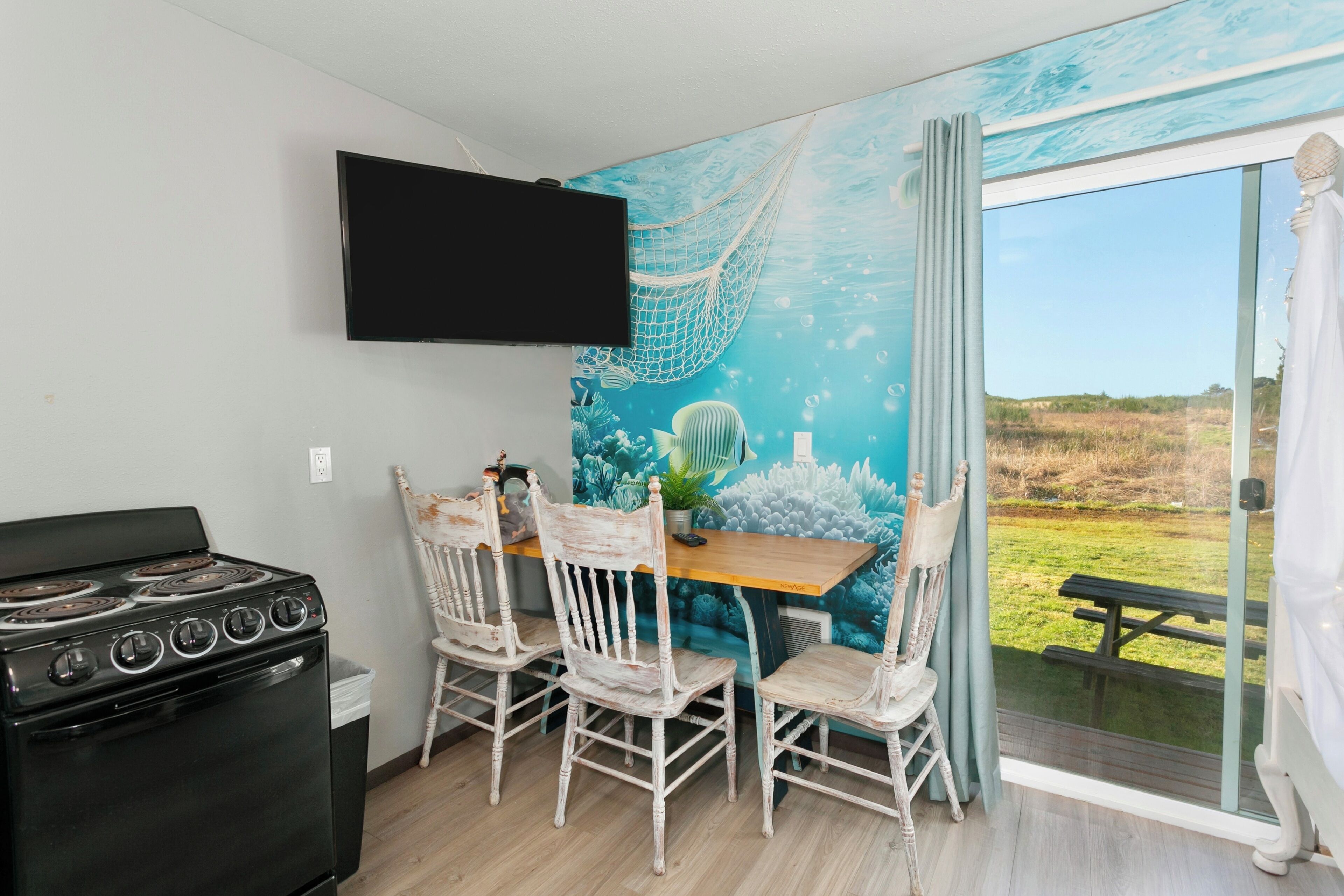 A kitchen with a stove, a dining table with chairs, a mural of an underwater scene, and a large window with a view of the outdoors.
