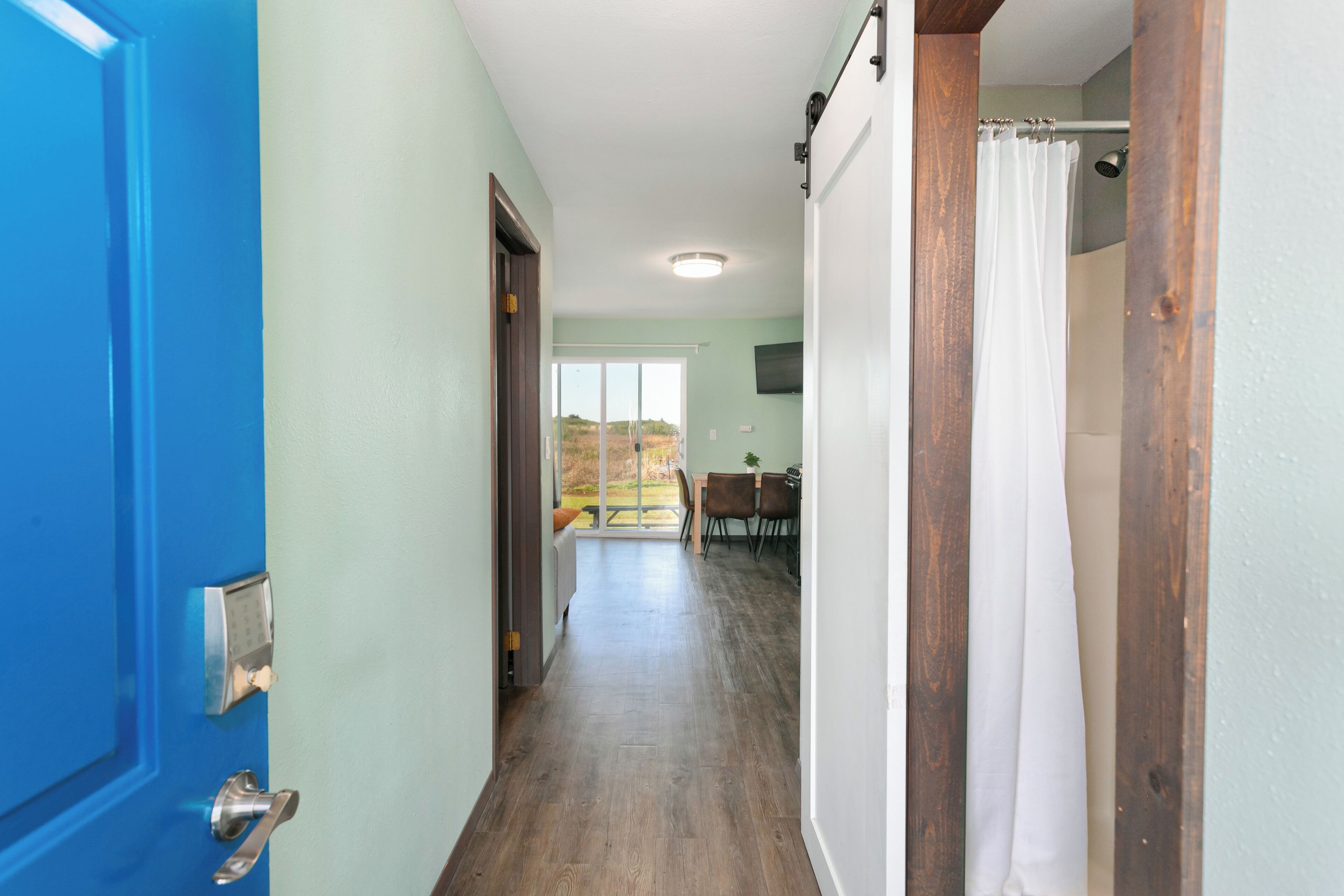 Un couloir avec une porte bleue, un chambranle en bois et un rideau blanc.