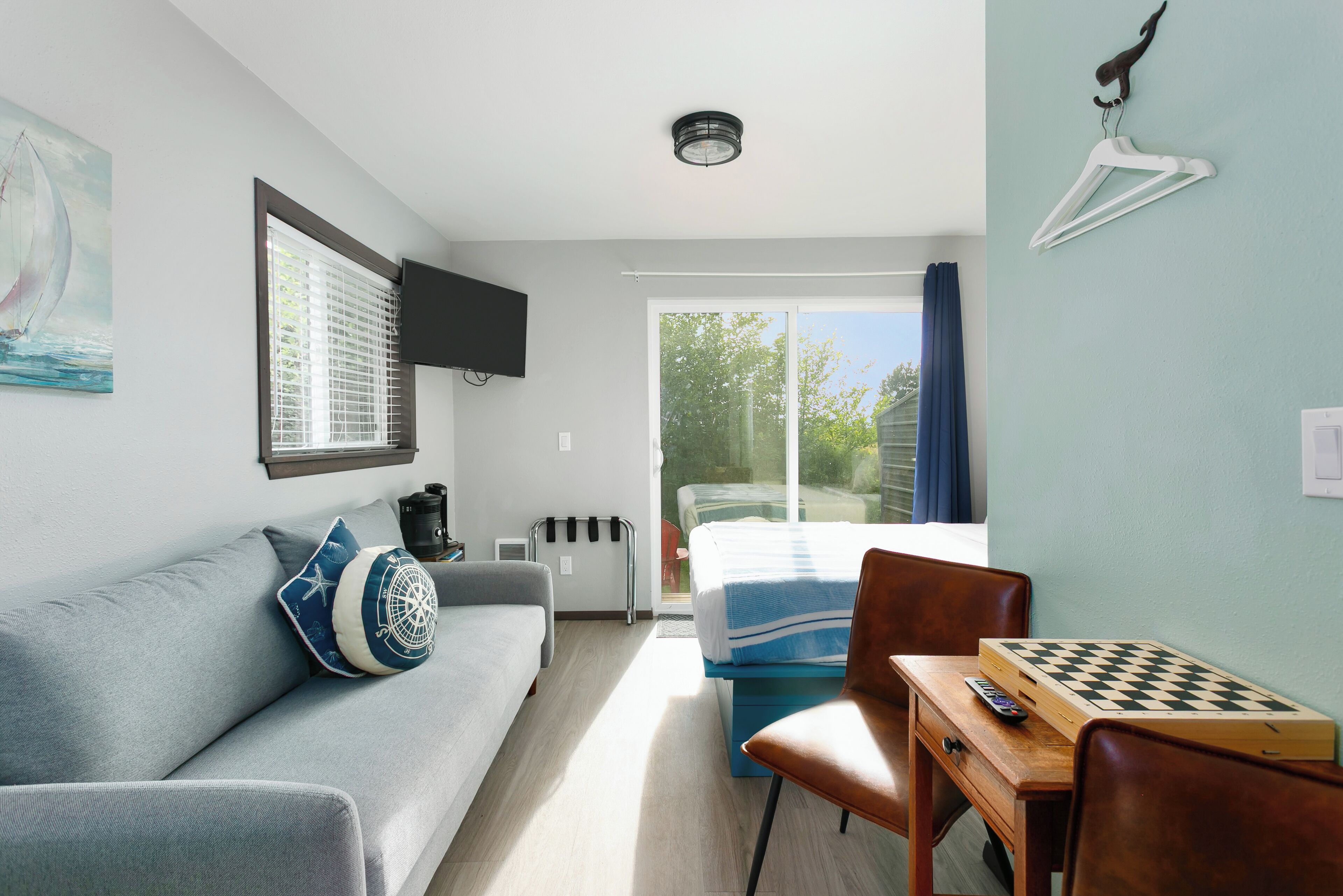 A modern room with a sofa, a small table with a chessboard, a TV mounted on the wall, and a window with blinds.
