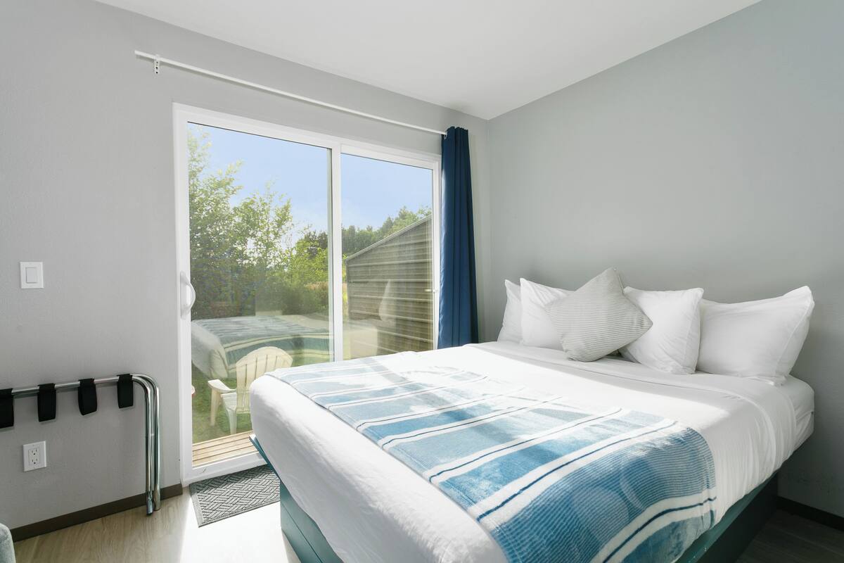 A bedroom with a bed, a sliding glass door to the outside, and a small table by the door.