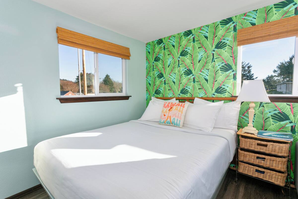 A bedroom with a bed, a nightstand, a lamp, and a window with a view.