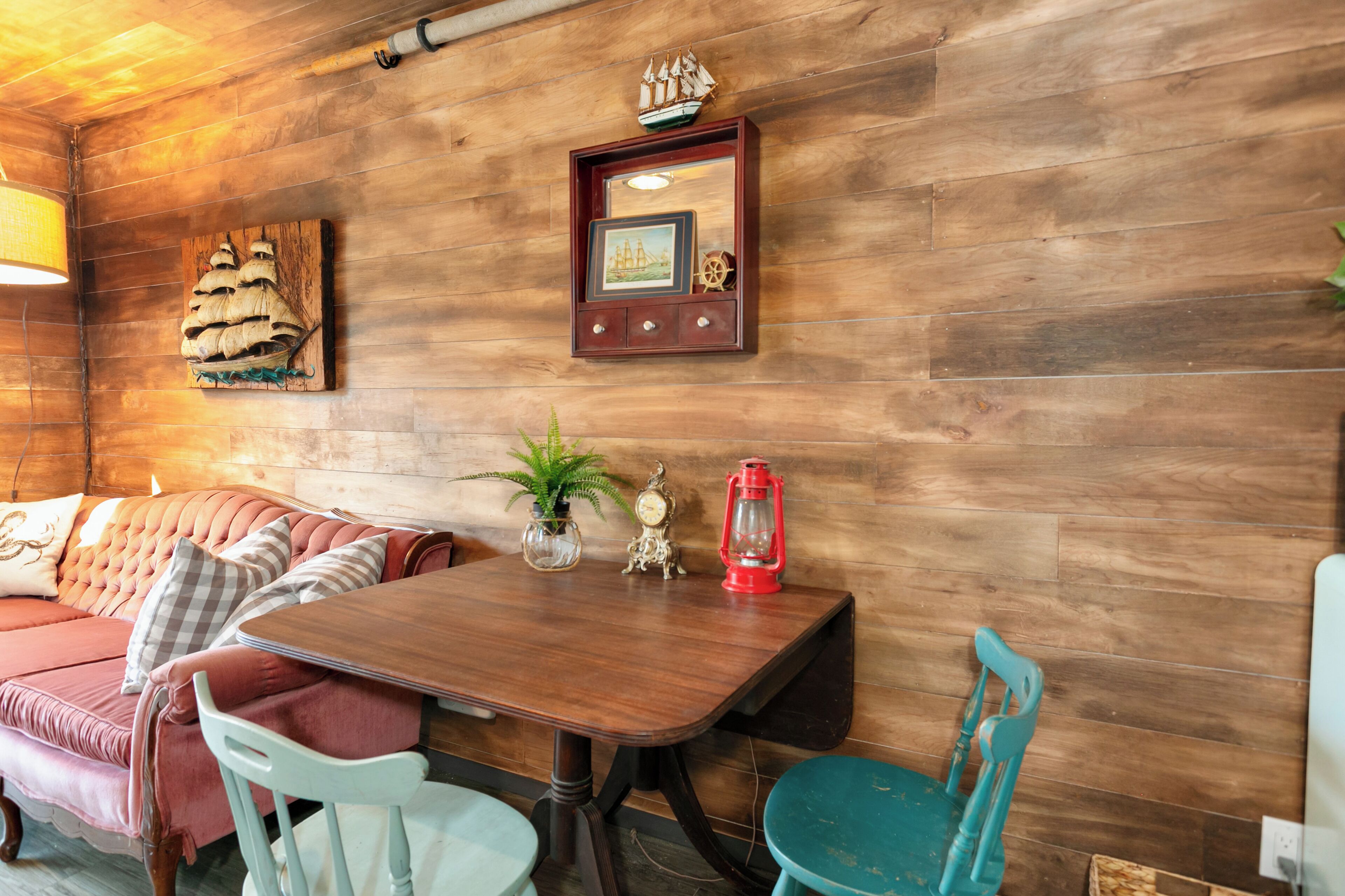 Une pièce chaleureuse avec un mur en bois, une table en bois, un canapé rose et un fauteuil turquoise.