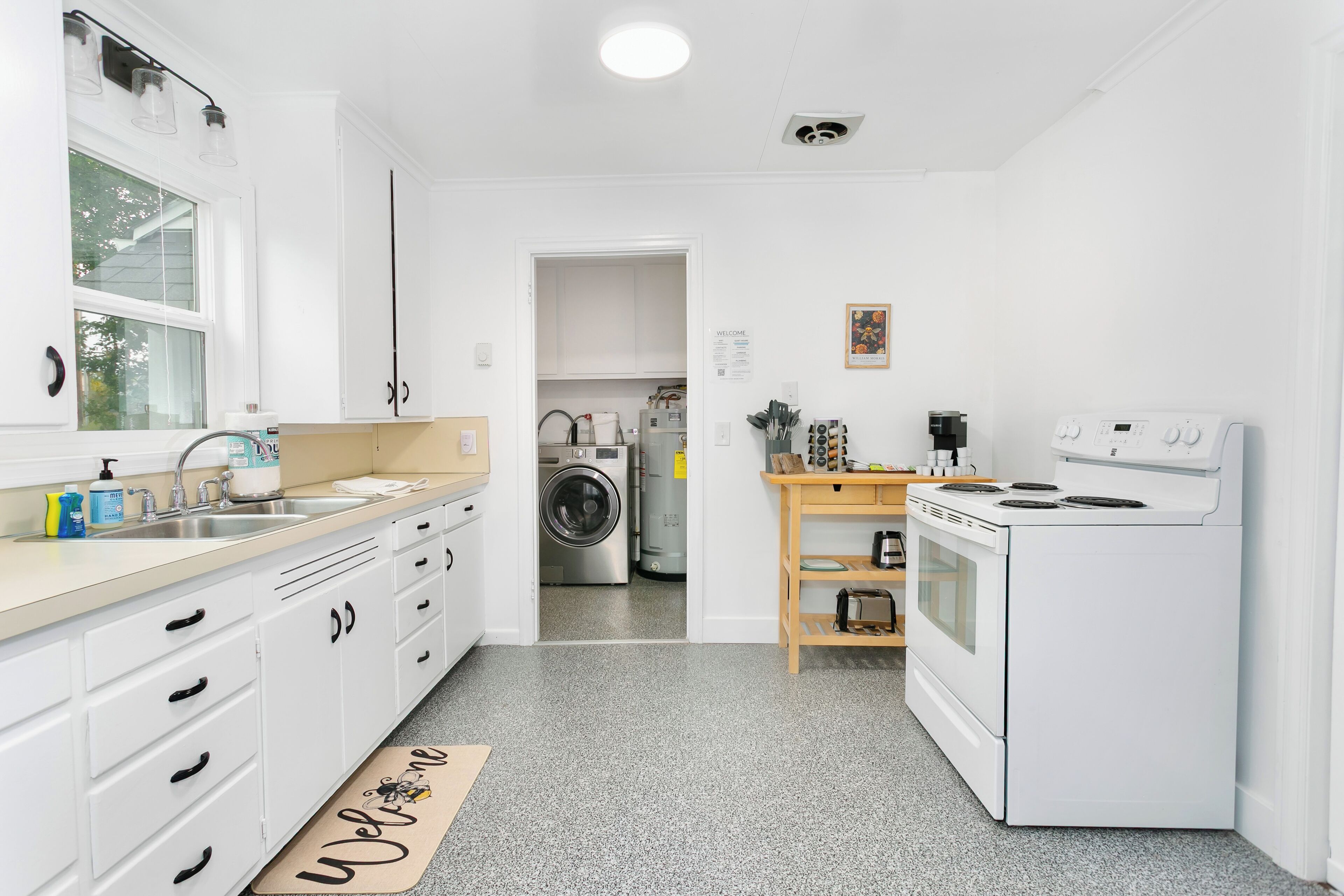A modern kitchen with white cabinetry, a stainless steel sink, a built-in washing machine, and a white stove.