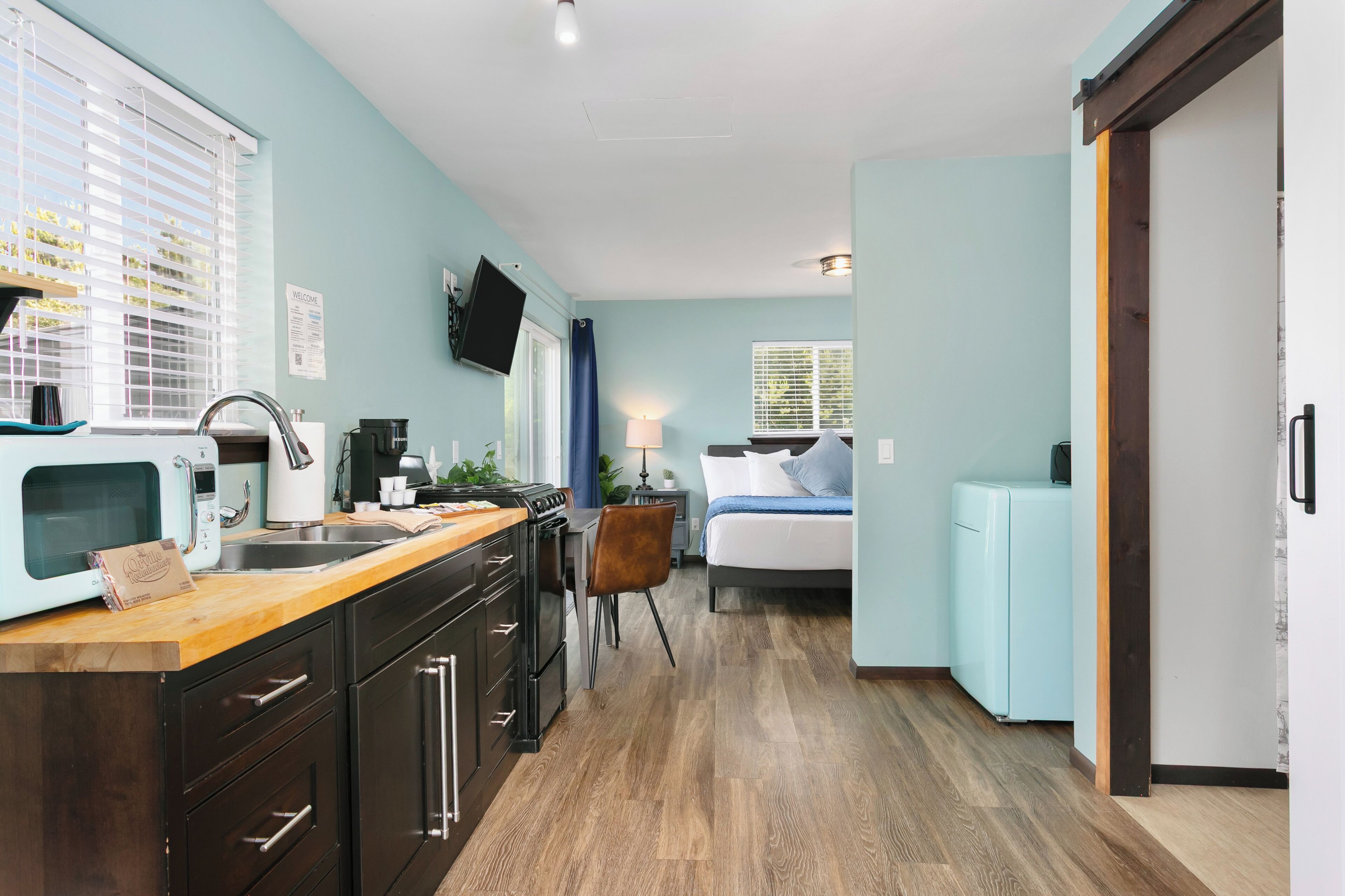 A compact kitchen with a wooden countertop, dark cabinets, and a built-in microwave.