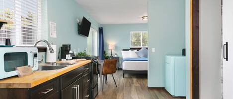 A compact kitchen with a wooden countertop, dark cabinets, and a built-in microwave.