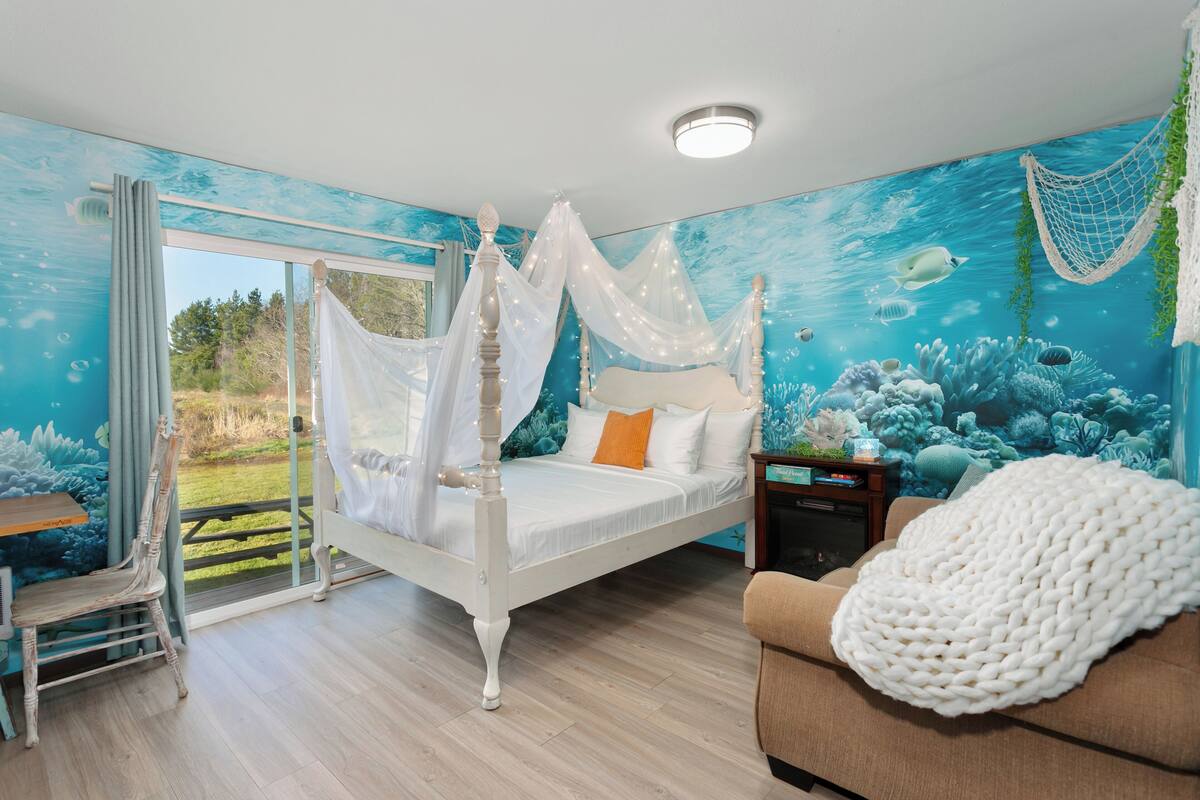 A bedroom with a four-poster bed, a small table, and a sofa.