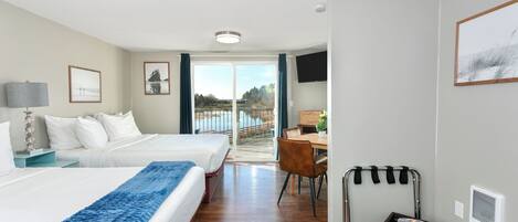 A hotel room with two beds, a desk, a chair, a TV, and a view of the outdoors.