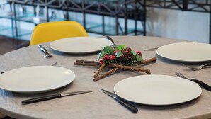 Una mesa redonda de comedor con platos blancos, cubiertos y un centro de mesa decorado con piñas, bayas y follaje.