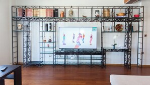Una sala de estar con un televisor sobre un mueble negro de metal, rodeada de estanterías de vidrio con libros y objetos decorativos.
