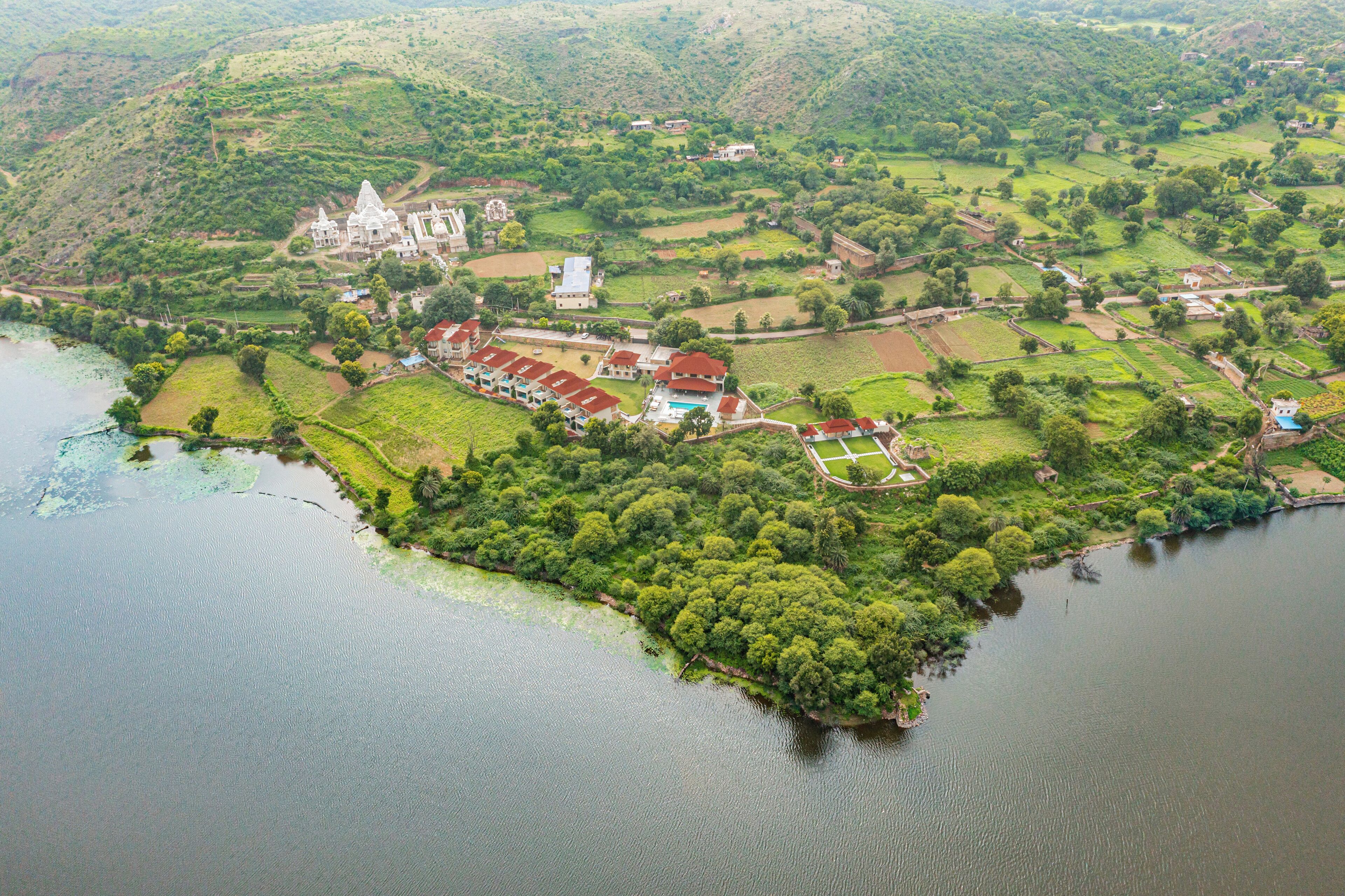 An aerial view of a coastal area with a large building, possibly a resort or hotel, surrounded by lush greenery and fields.