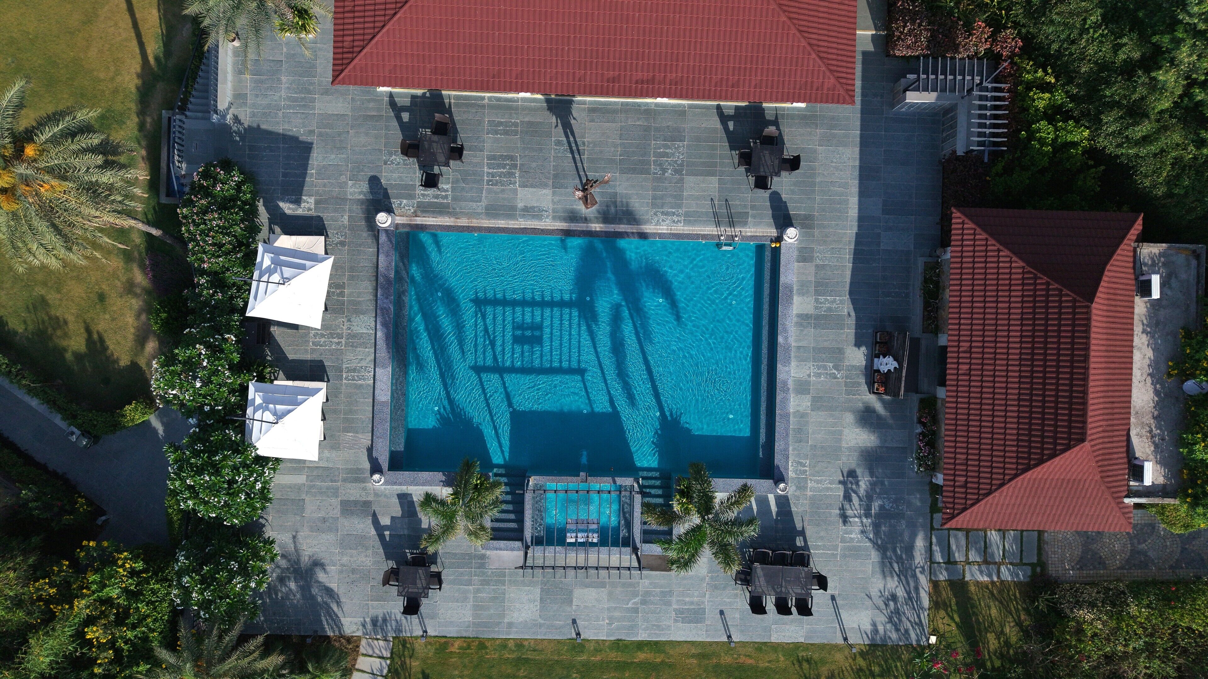 An aerial view of a swimming pool area with a tiled deck, lounge chairs, and umbrellas.