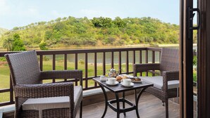 A balcony with wicker furniture, a table set with cups, a teapot, and pastries, overlooking a lush green landscape and a body of water. - Sarasiruham Resort - Private Pool Villa in Udaipur (Udaipur)