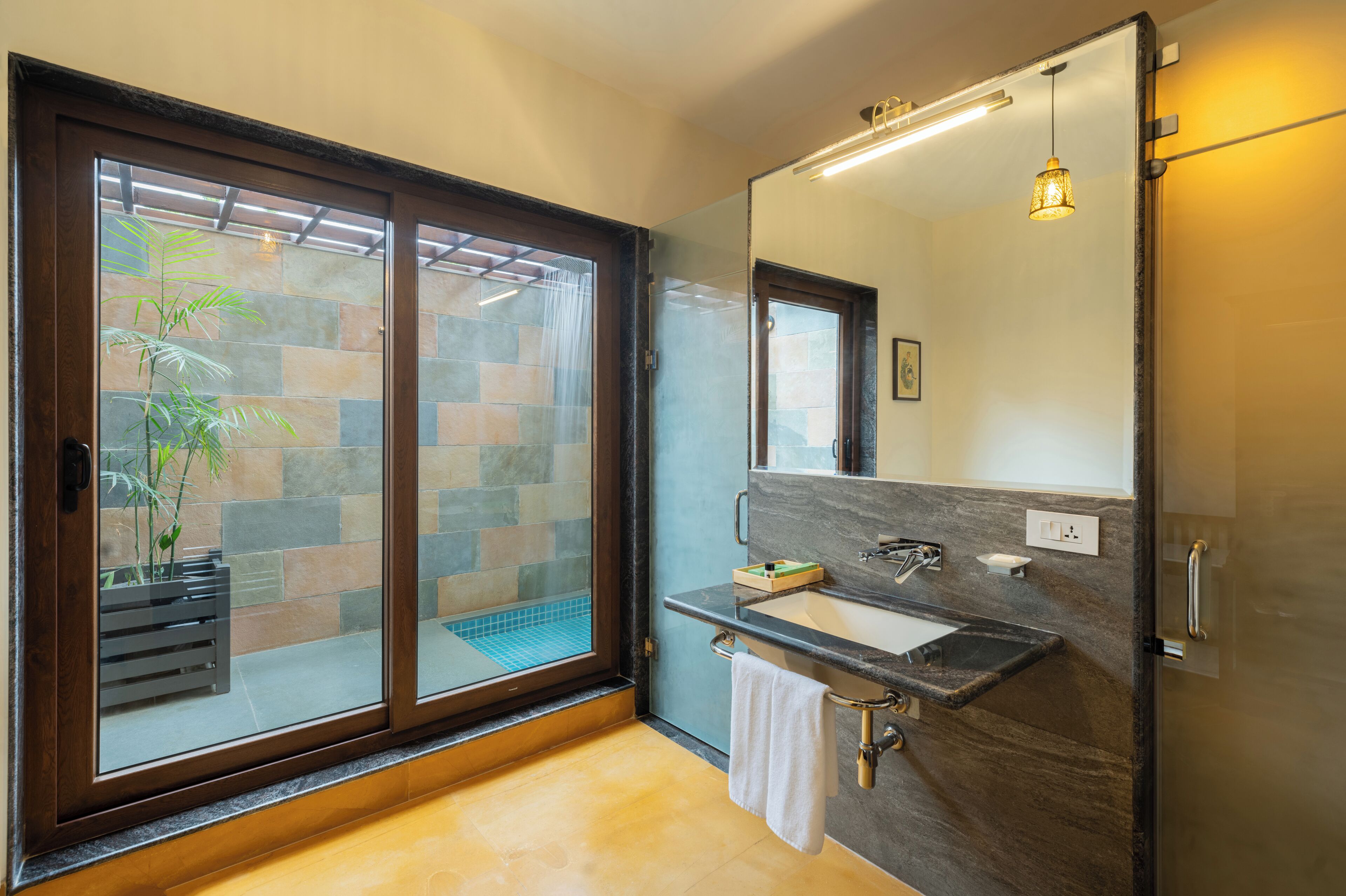 A modern bathroom with a glass door leading to a tiled area, a sink with a marble countertop, and a large mirror.