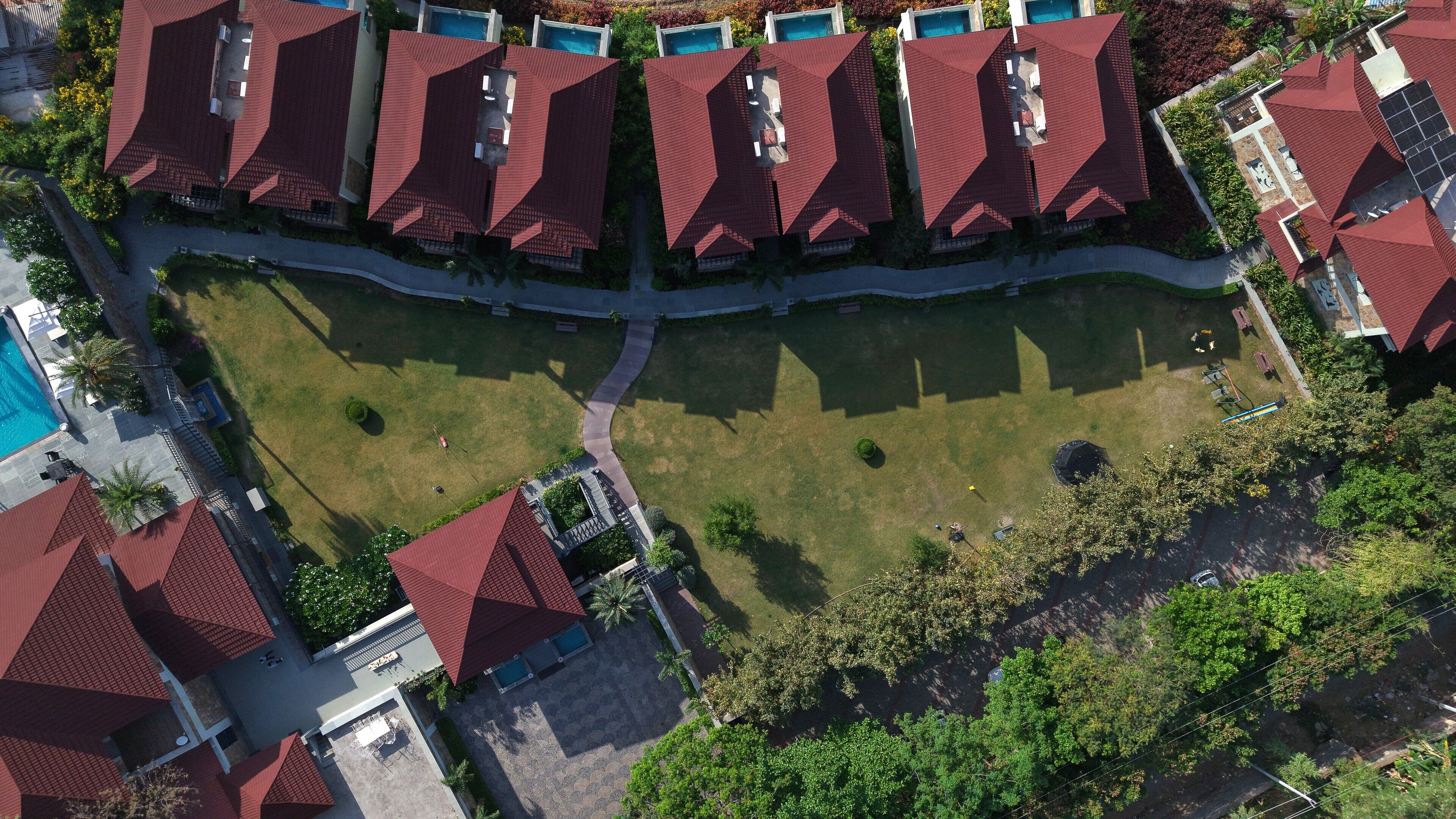 A residential area with multiple houses featuring red roofs, a central grassy area, and a swimming pool.