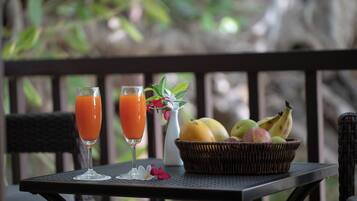 A table with two glasses of orange juice, a wicker basket with fruits, and a vase with flowers on a balcony.