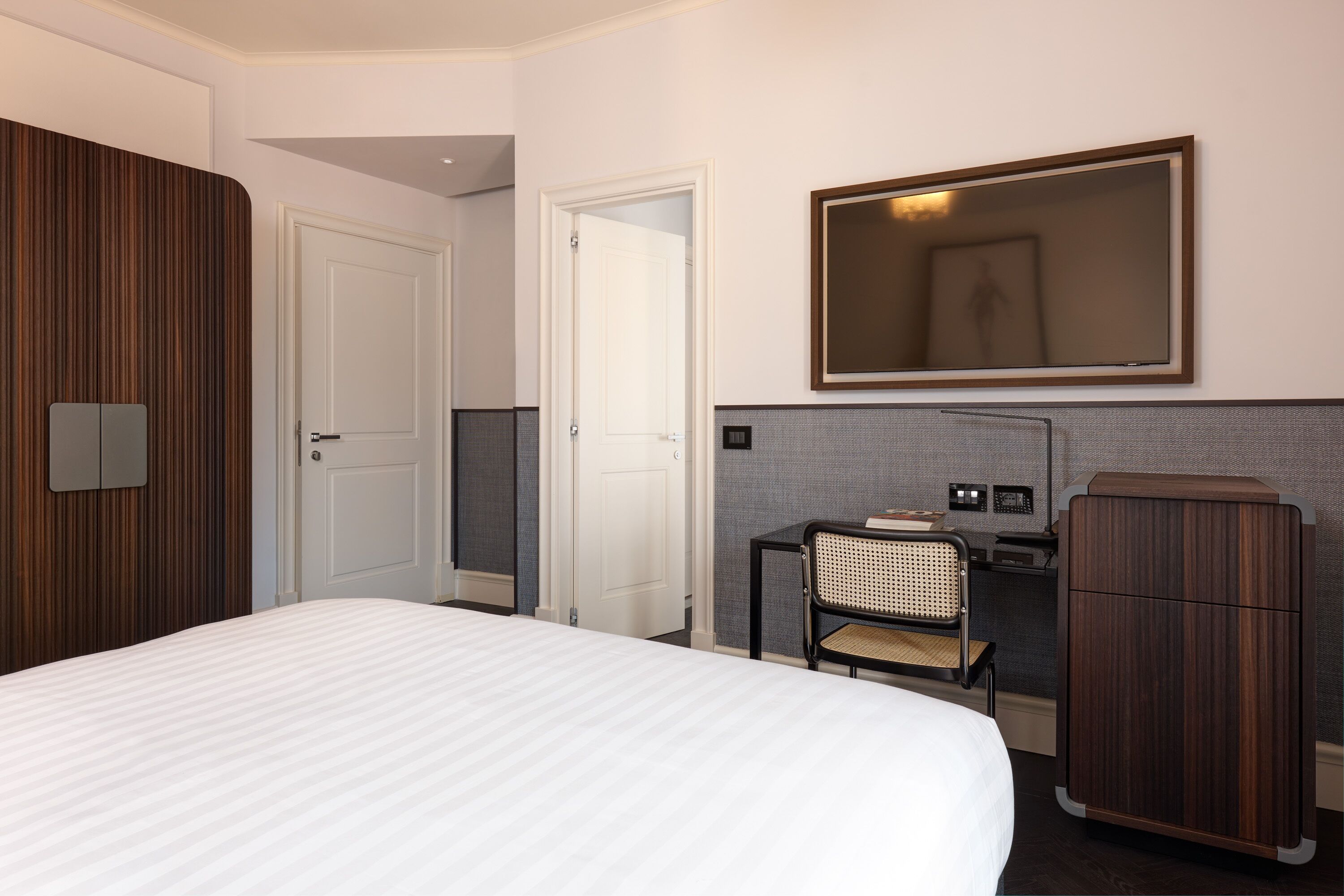 A hotel room with a large bed, a desk with a chair, a wardrobe, and a mirror on the wall.