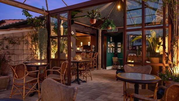 Un patio al aire libre con mobiliario de mimbre, mesas de vidrio y plantas en macetas.