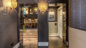 Un pasillo con una escalera que lleva a un área de bar, un aplique en la pared y una puerta con un letrero de número.