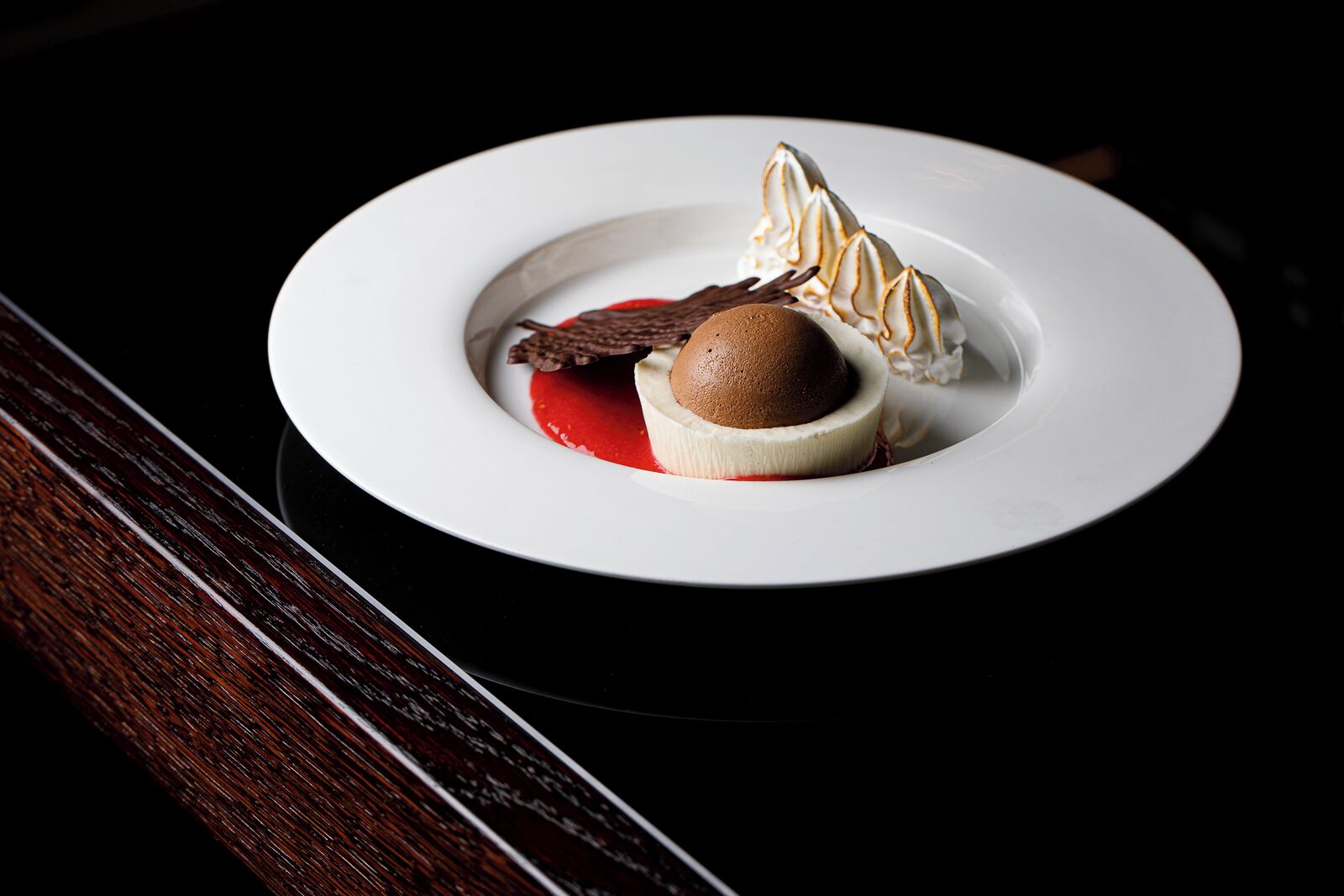 Un postre sobre un plato blanco, con un trozo de chocolate y una cucharada de crema.