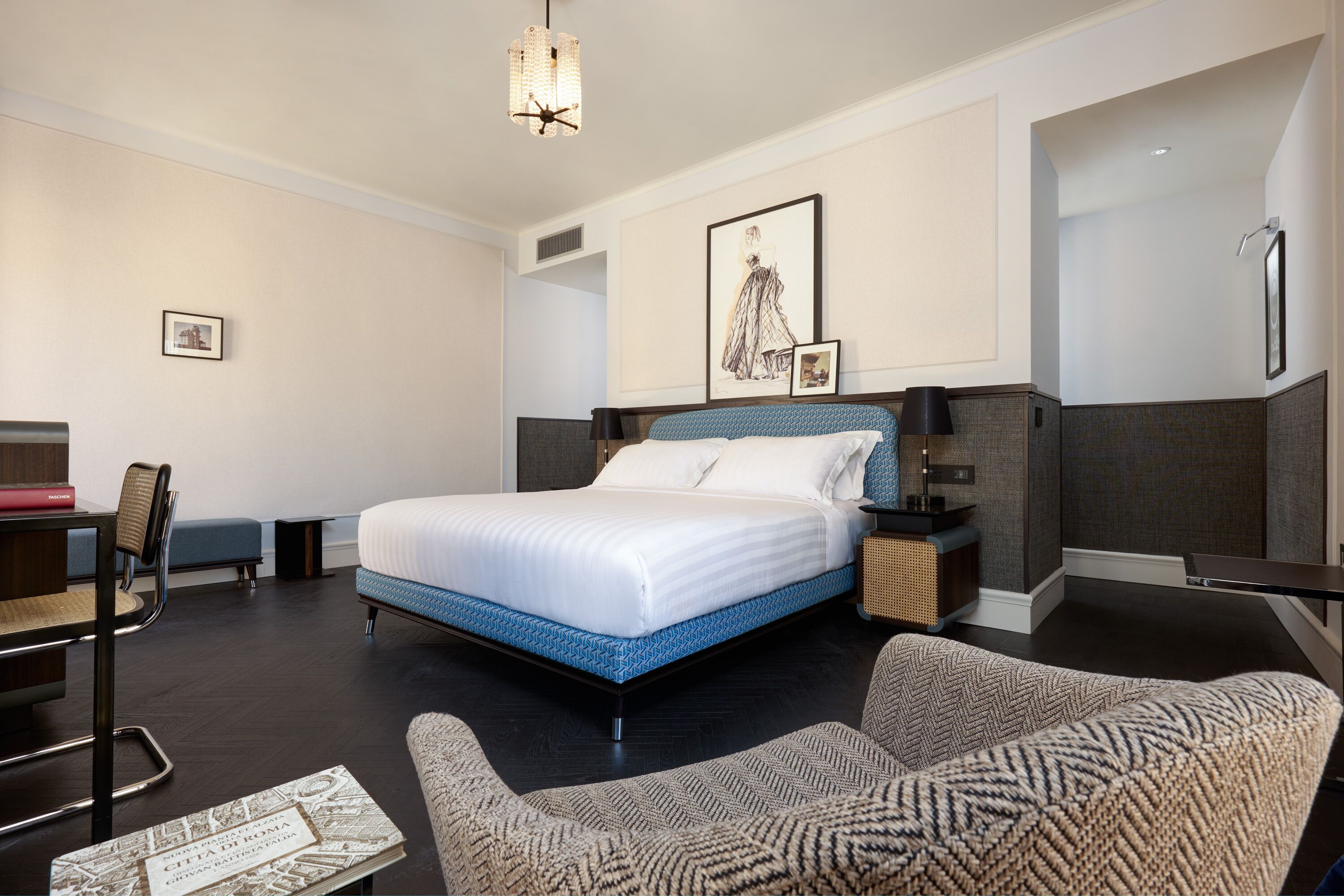 Een hotelkamer met een groot bed, een bureau, een stoel en een bank. Er hangt een lijst op de muur en op het nachtkastje staat een lamp.