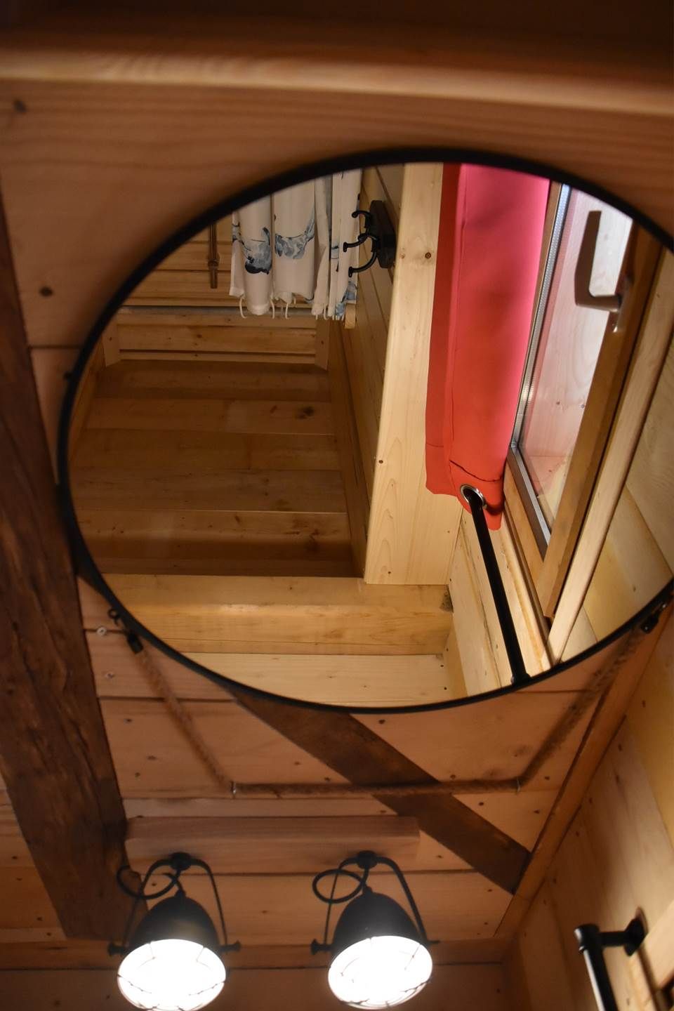 A wooden staircase with a circular mirror reflecting a red wall and a window.