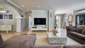 Ein geräumiges Wohnzimmer mit einem großen Flachbildfernseher, einem Marmortisch und zwei Sofas.