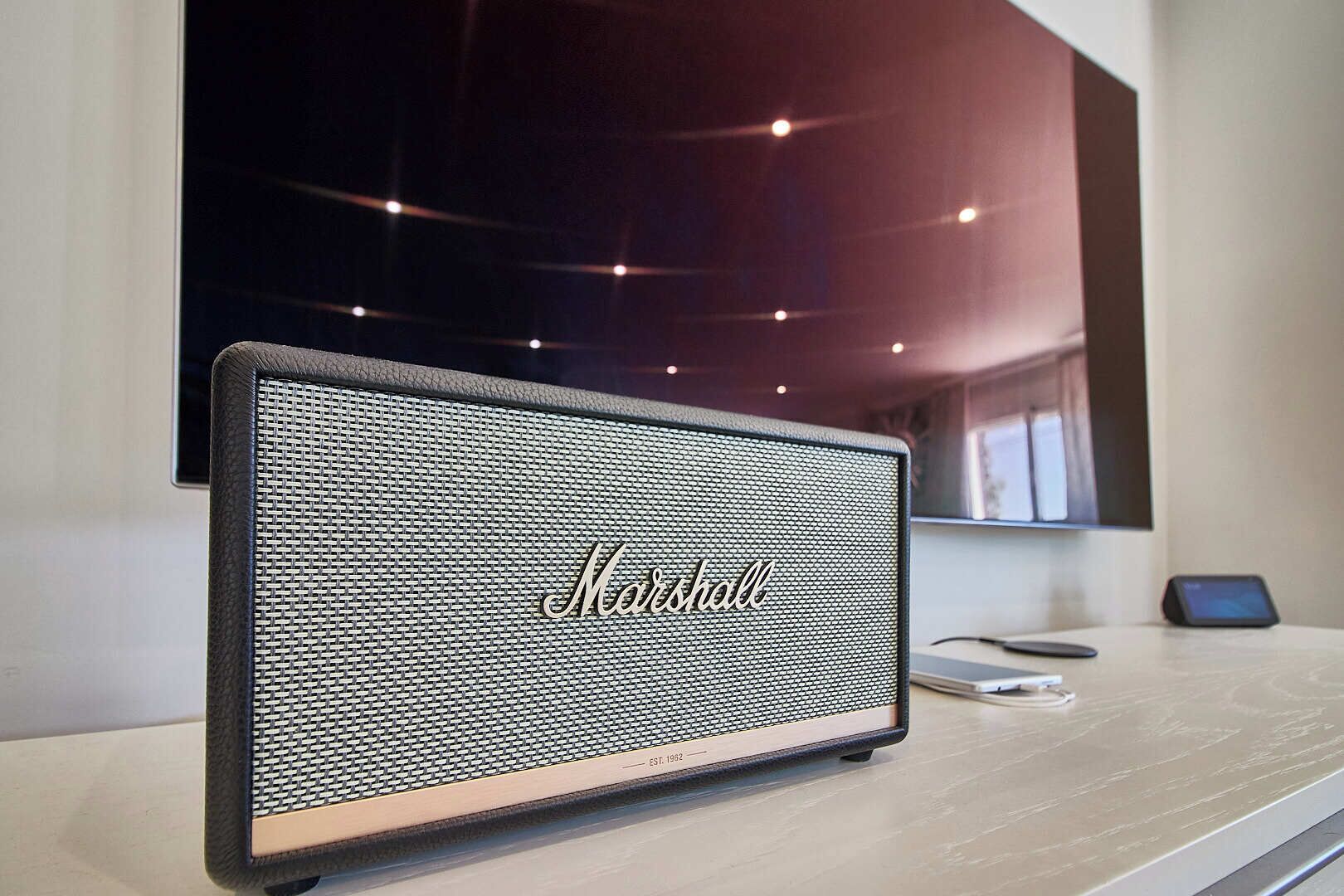 Un altavoz Marshall sobre una mesa de madera en una habitación moderna con techo oscuro y una ventana.