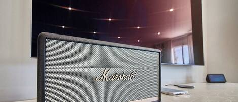 Un altavoz Marshall sobre una mesa de madera en una habitación moderna con techo oscuro y una ventana.