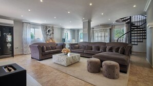 Ein geräumiges Wohnzimmer mit einer großen Eckcouch, einem Marmortisch und einer schwarzen Treppe.