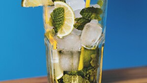 A glass with ice, mint leaves, and a slice of lemon, with a purple and yellow straw. - Roomshala 061 NK Residency (New Delhi)