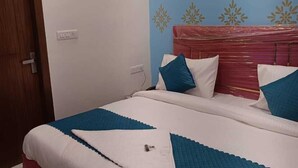 A bedroom with a bed, a wooden door, and a wall with a floral pattern. - Roomshala 061 NK Residency (New Delhi)