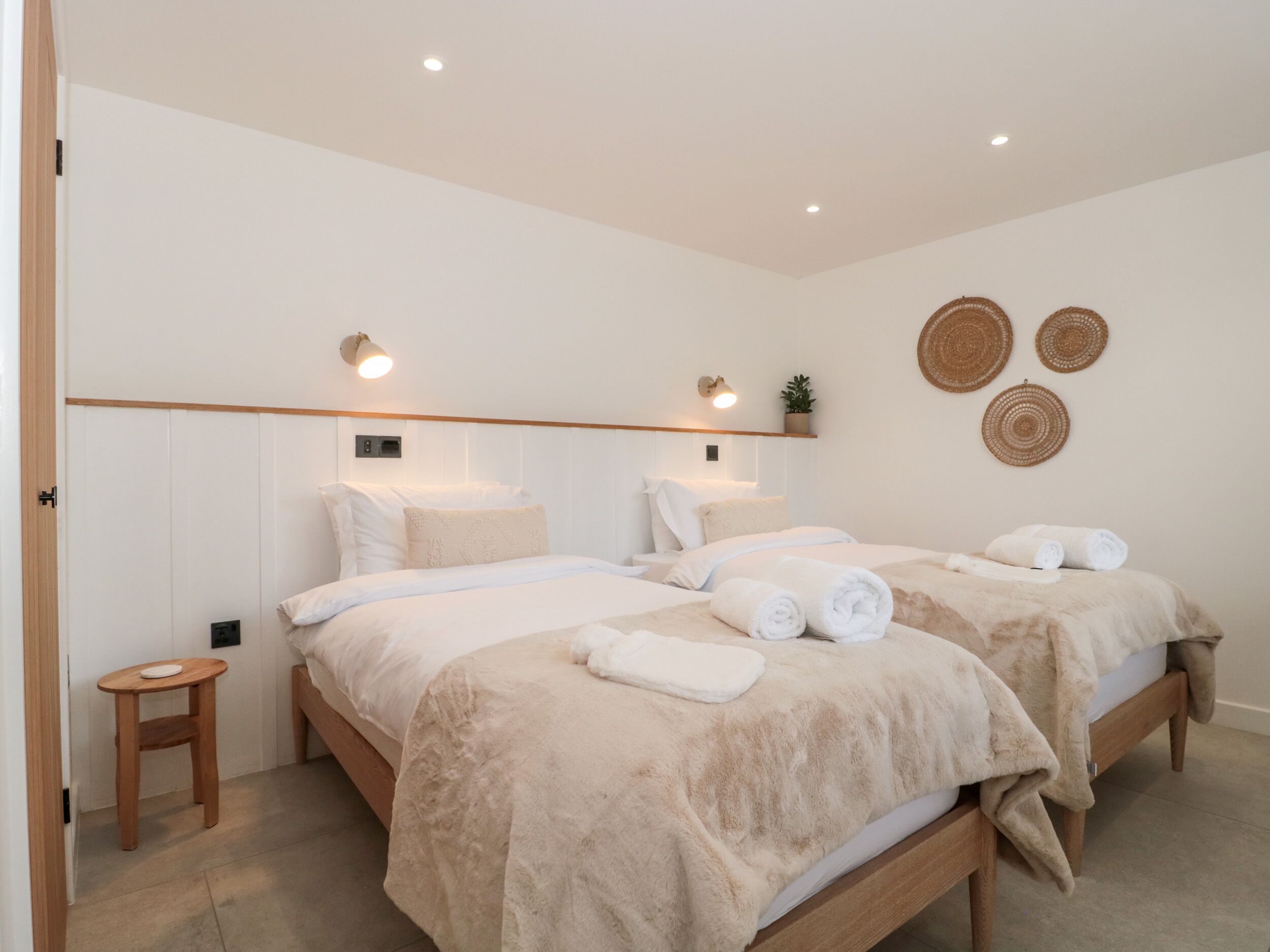 A modern bedroom with two beds, a small bedside table, and a wall-mounted shelf with a plant.