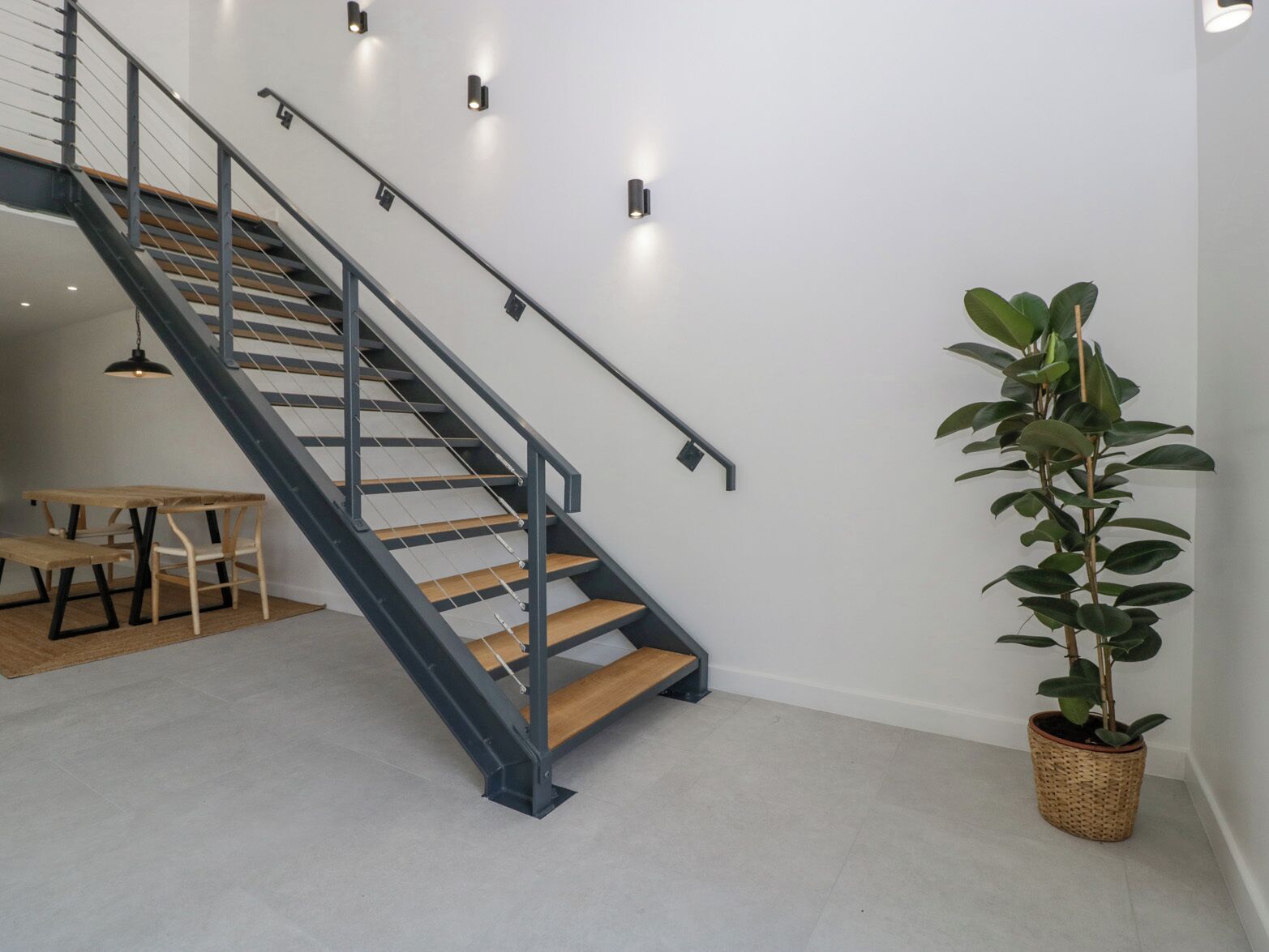 Una escalera con escalones de madera y barandillas de metal, una pequeña mesa con bancos y una planta en maceta.