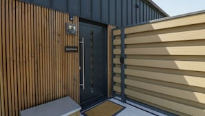 Un bâtiment moderne à la façade sombre, doté d’une entrée avec des lambris en bois et d’un banc à l’extérieur.