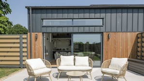 Une terrasse extérieure avec des meubles en osier, une porte-fenêtre coulissante donnant sur la cuisine et une clôture en bois.