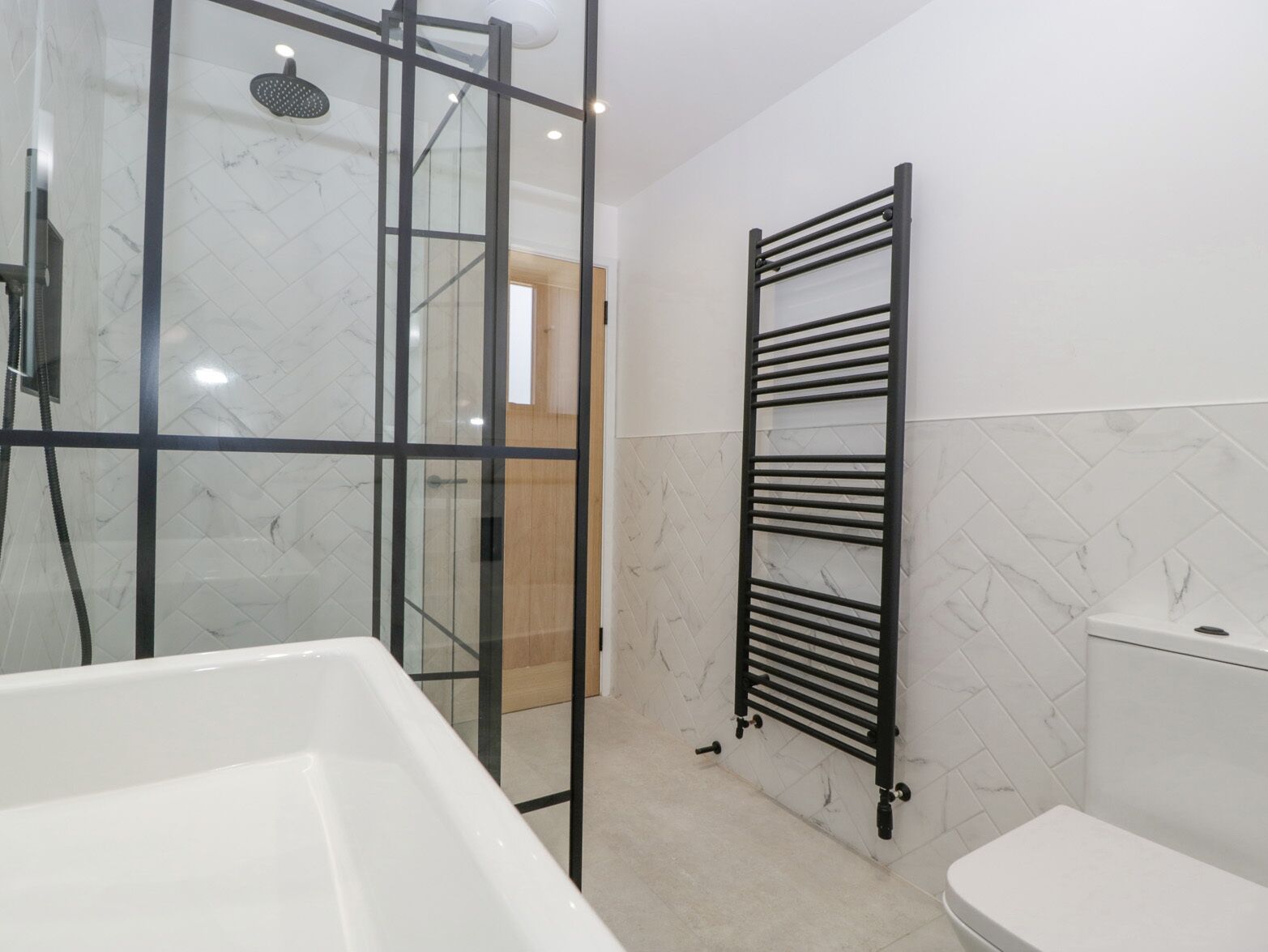 A modern bathroom with a glass shower enclosure, a white bathtub, and a black towel rack.