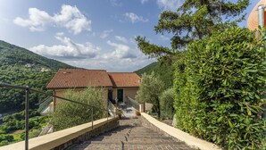 A stone staircase leading to a building with a red-tiled roof, surrounded by greenery and hills. - Belvedere – Avegno (Avegno)