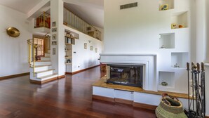 A spacious living area with a fireplace, wooden flooring, a staircase with a railing, and a bookshelf. - Belvedere – Avegno (Avegno)