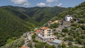 A hillside village with traditional architecture, including a prominent building with a balcony and a swimming pool. - Belvedere – Avegno (Avegno)