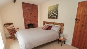 Un dormitorio con chimenea de ladrillo, una mecedora de madera, una cama con almohadas y una puerta de madera.